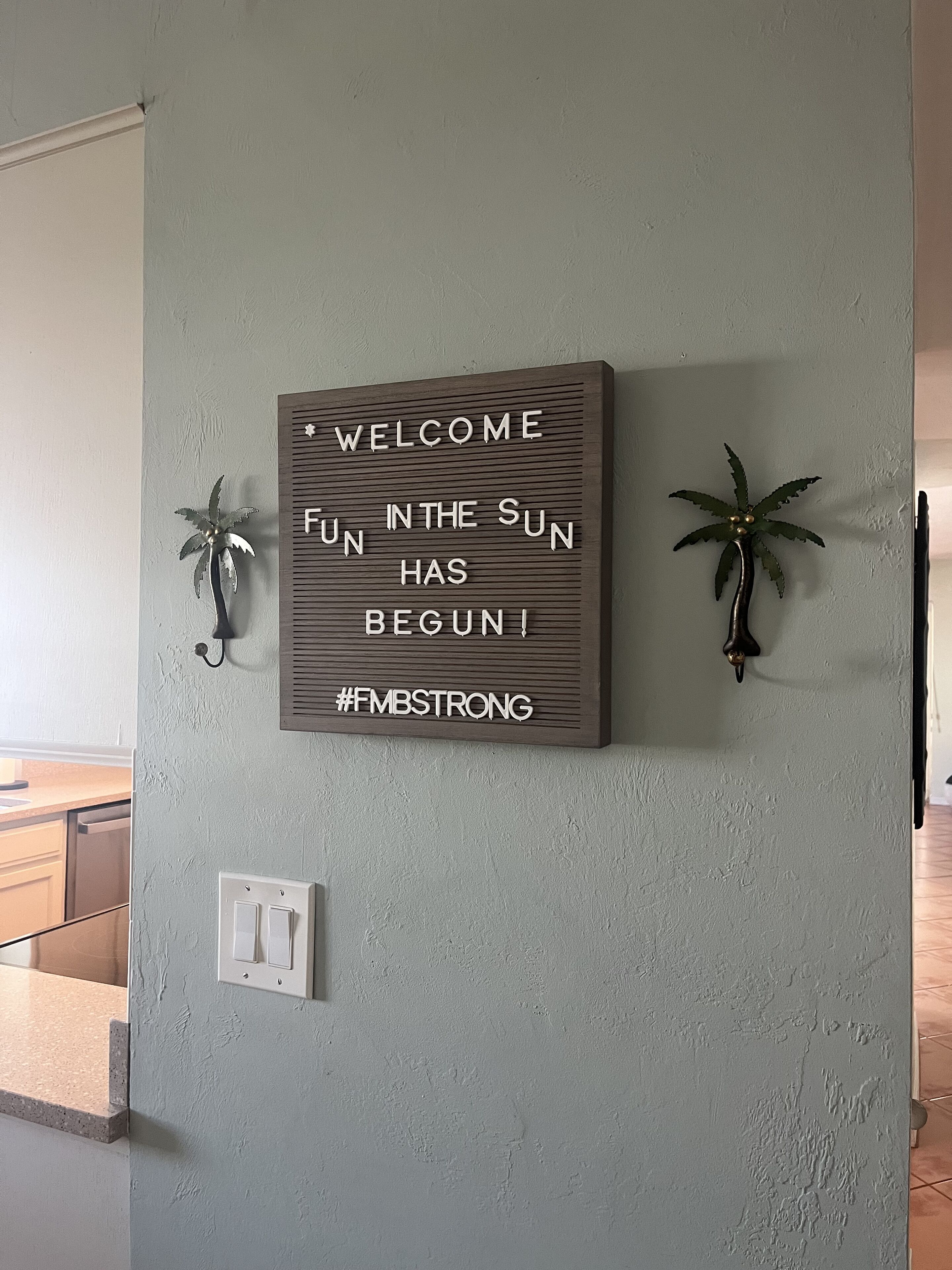 Ein an der Wand befestigtes Schild mit motivierenden Text und dekorativen Zimmerpalmen.