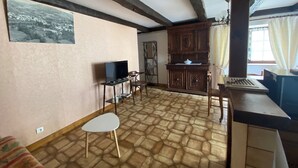 Une pièce avec un sol carrelé, un téléviseur posé sur une petite table, un meuble et une fenêtre avec des rideaux.