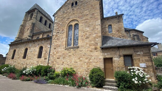 Un bâtiment historique en pierre, doté d’une tour imposante et de fenêtres en arc de cercle, entouré de jardins bien entretenus.