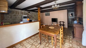 Une cuisine rustique avec un mur en pierre, des poutres en bois, une table en bois et un téléviseur.