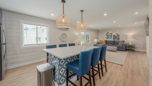 A modern kitchen with a white island, blue chairs, and pendant lights.