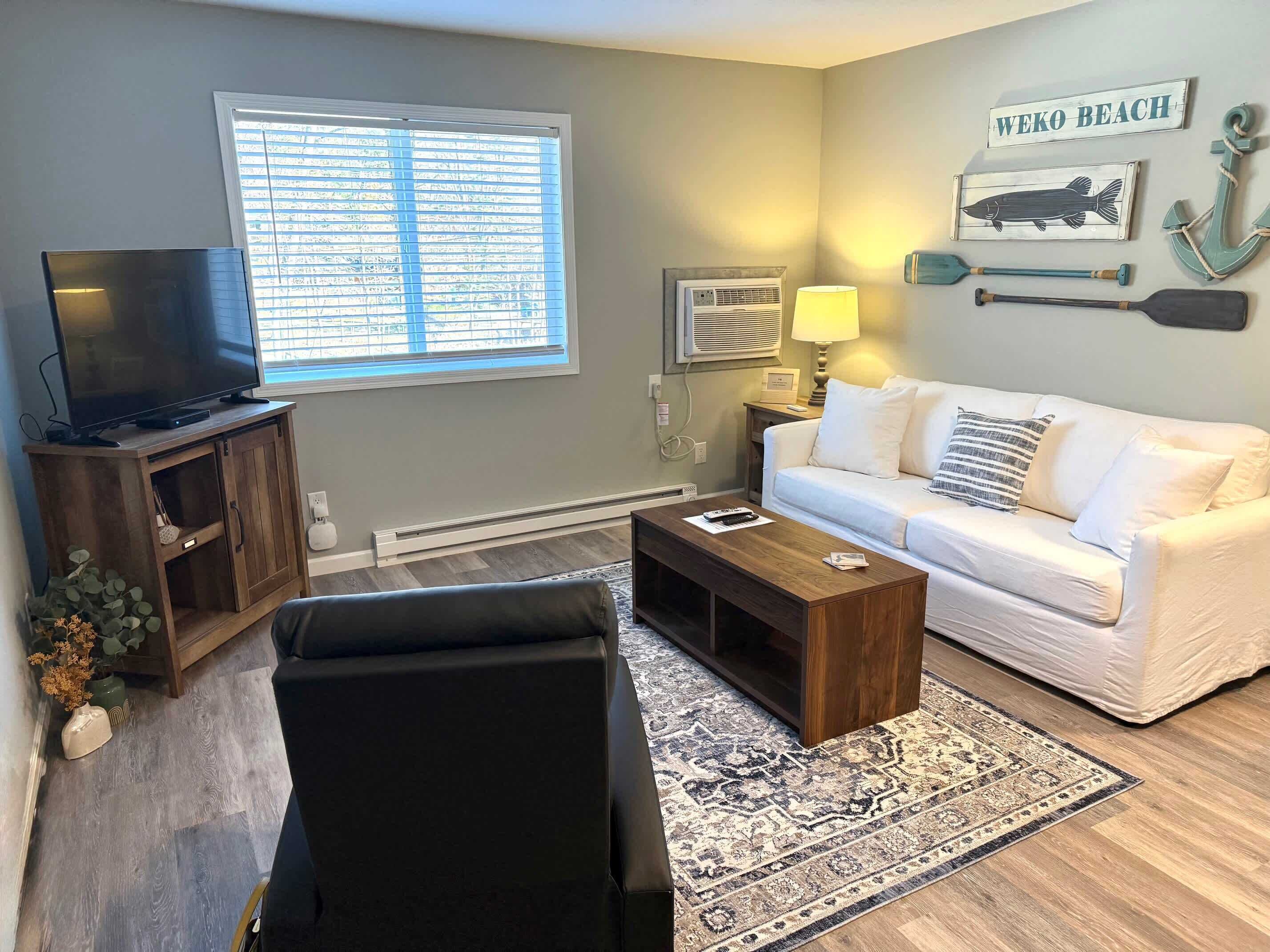 A living room with a TV, sofa, coffee table, and decorative items including a wall-mounted sign reading "WEKO BEACH".