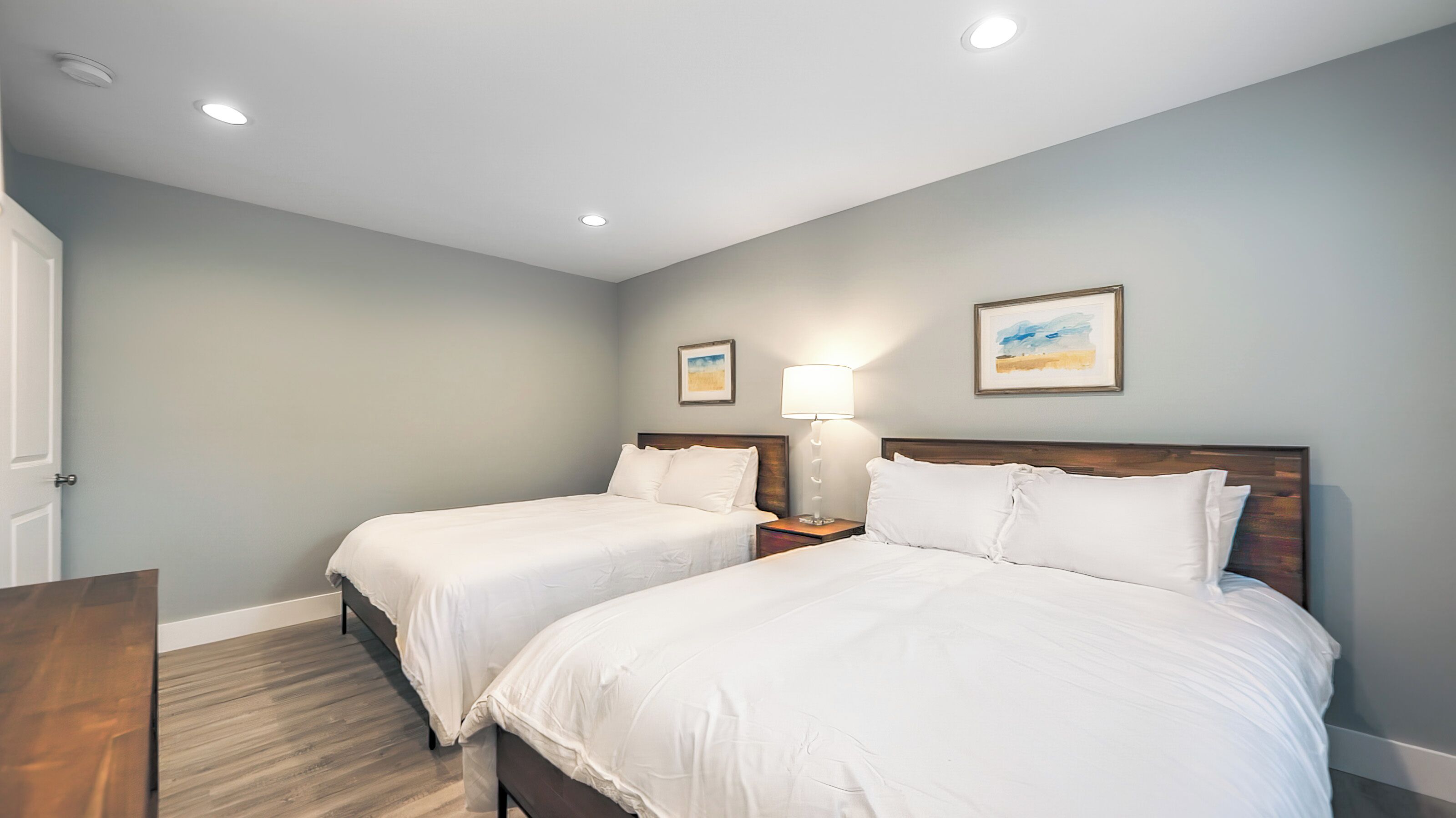 A hotel room with two beds, a wooden floor, and a ceiling with recessed lighting.