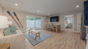 A spacious living area with a sofa, a dining table with chairs, a TV mounted on the wall, and a kitchen area with a refrigerator.
