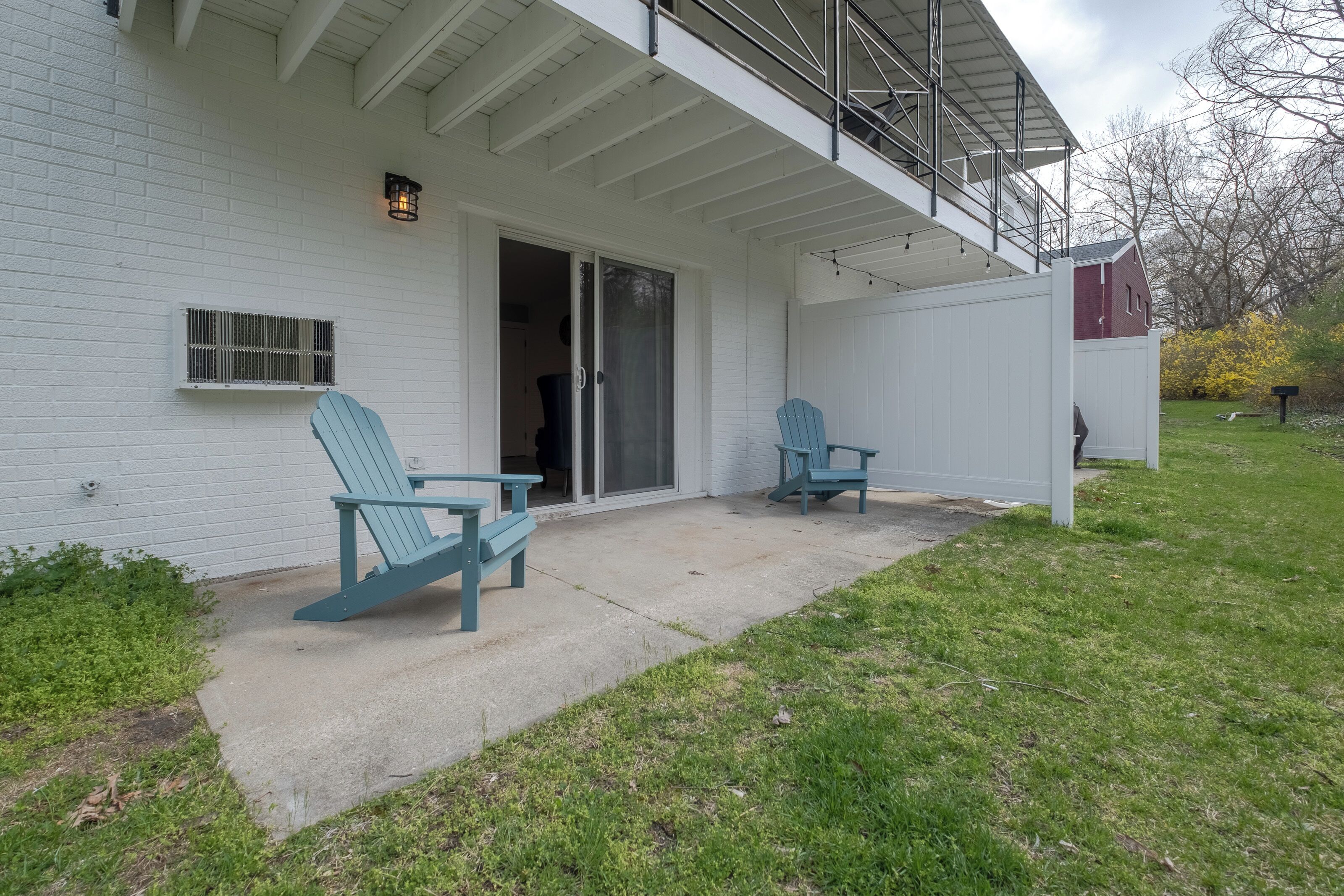 A white house with a covered patio, two blue Adirondack chairs, and a sliding glass door.