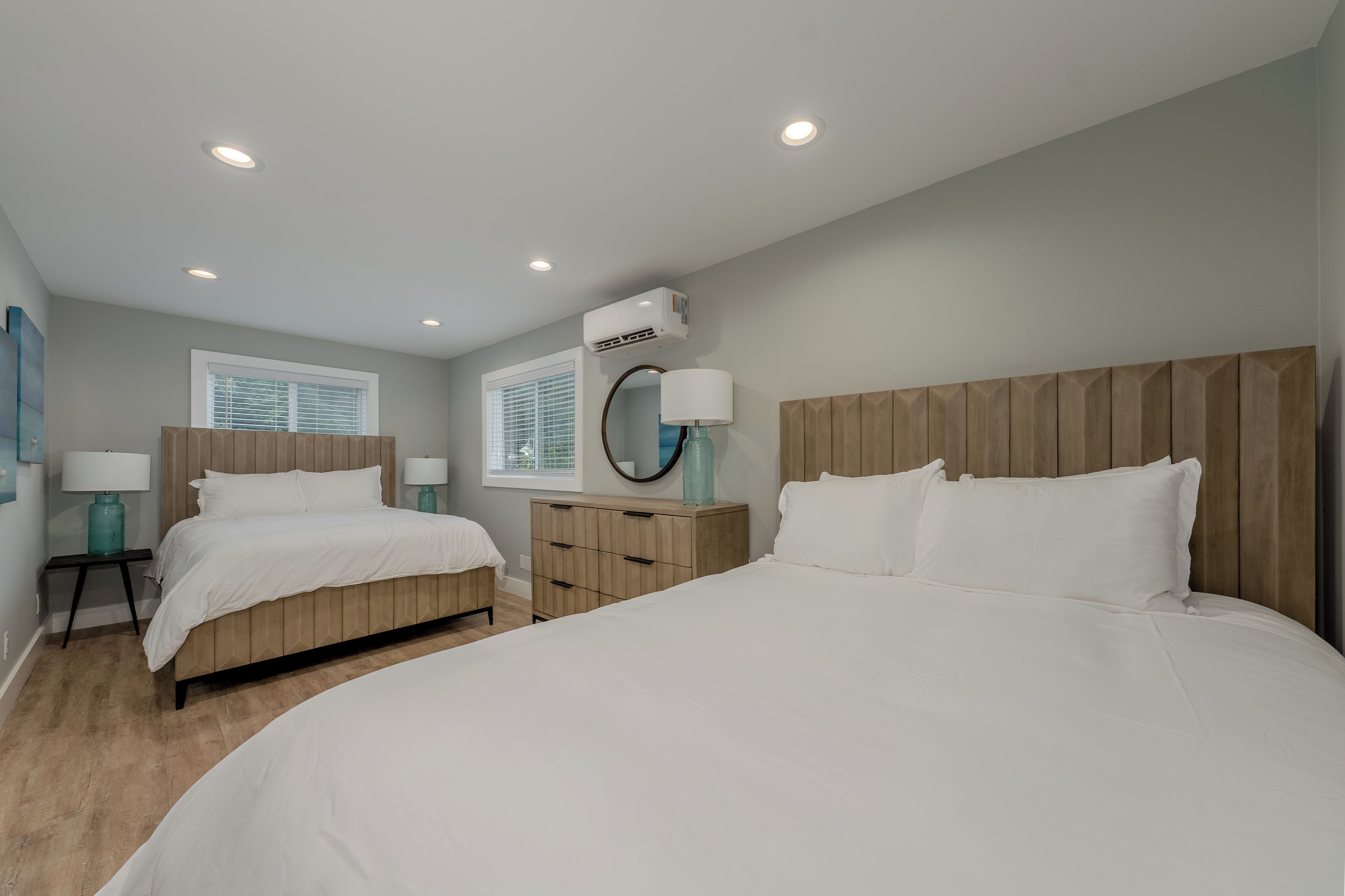 Une chambre avec deux lits, une tête de lit en bois, une table de chevet avec une lampe et une fenêtre avec des stores.