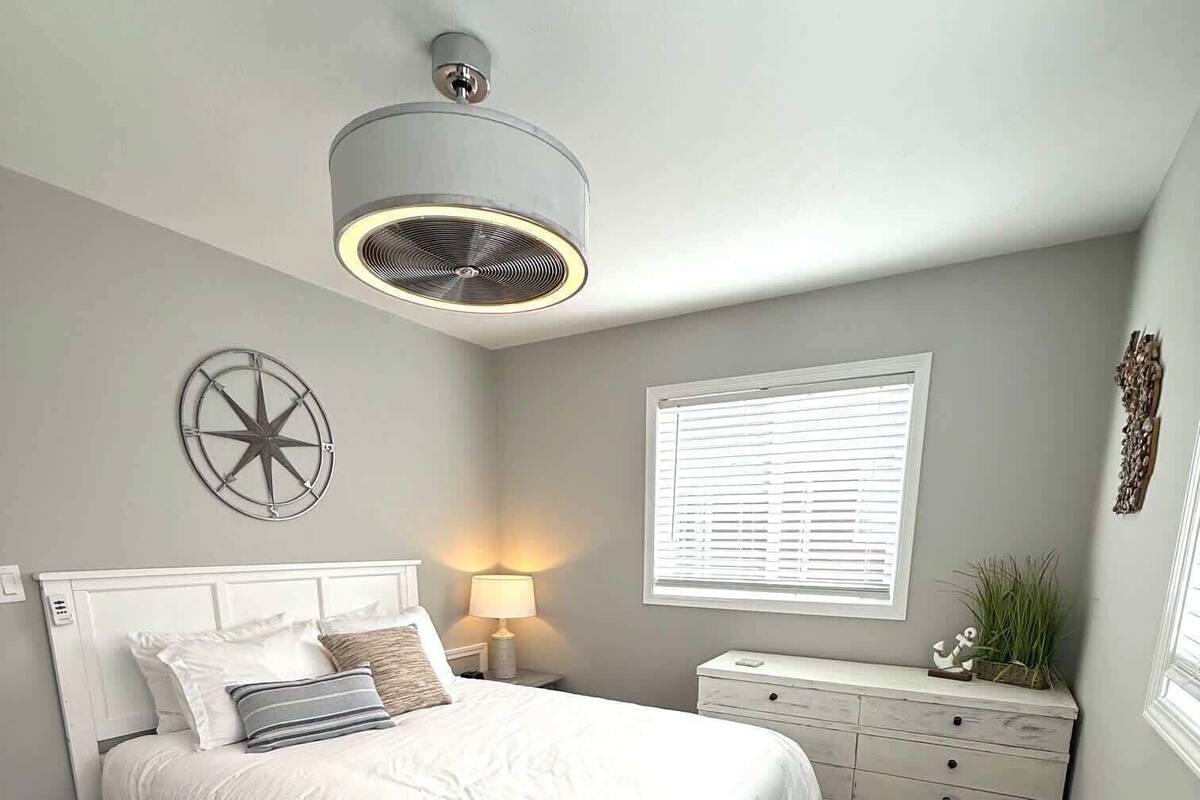 Une chambre à coucher comprenant un lit, une table de chevet, une lampe, une fenêtre et un élément décoratif mural.