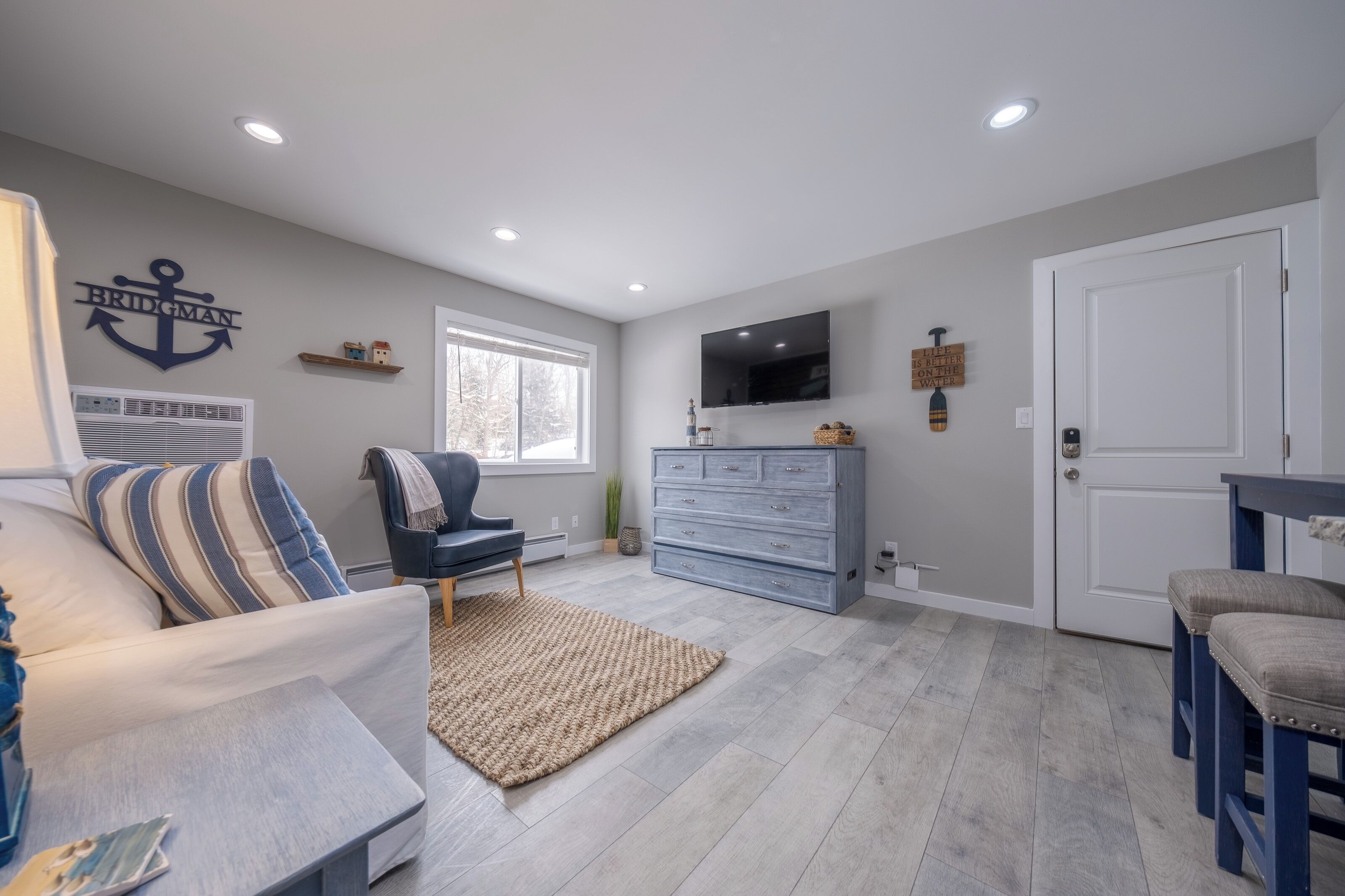 Un salon moderne comprenant un canapé, un fauteuil, un téléviseur, une commode et une porte.