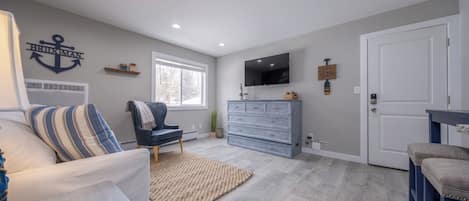 Un salon moderne comprenant un canapé, un fauteuil, un téléviseur, une commode et une porte.