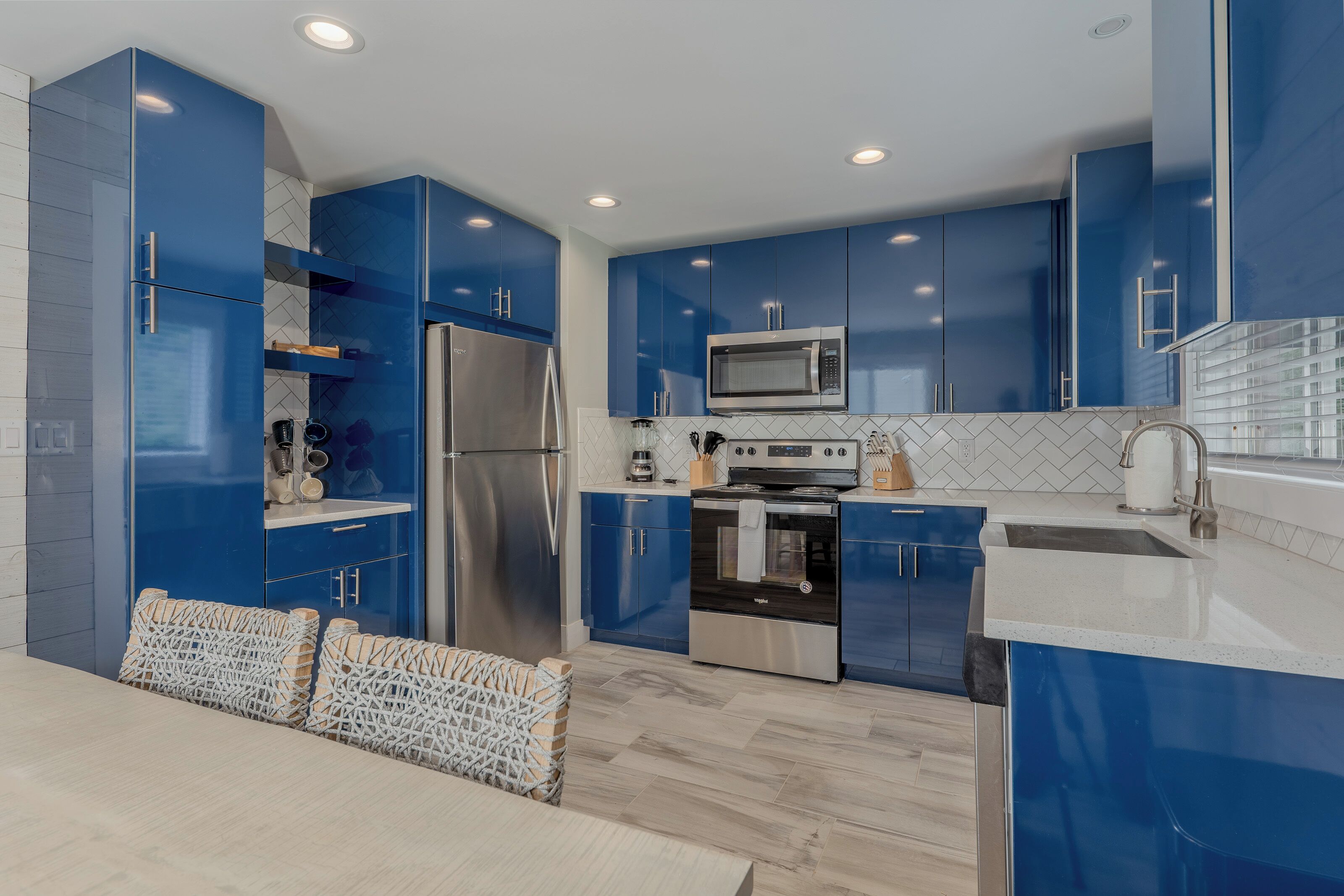 A modern kitchen with blue cabinets, stainless steel appliances, and a white countertop.