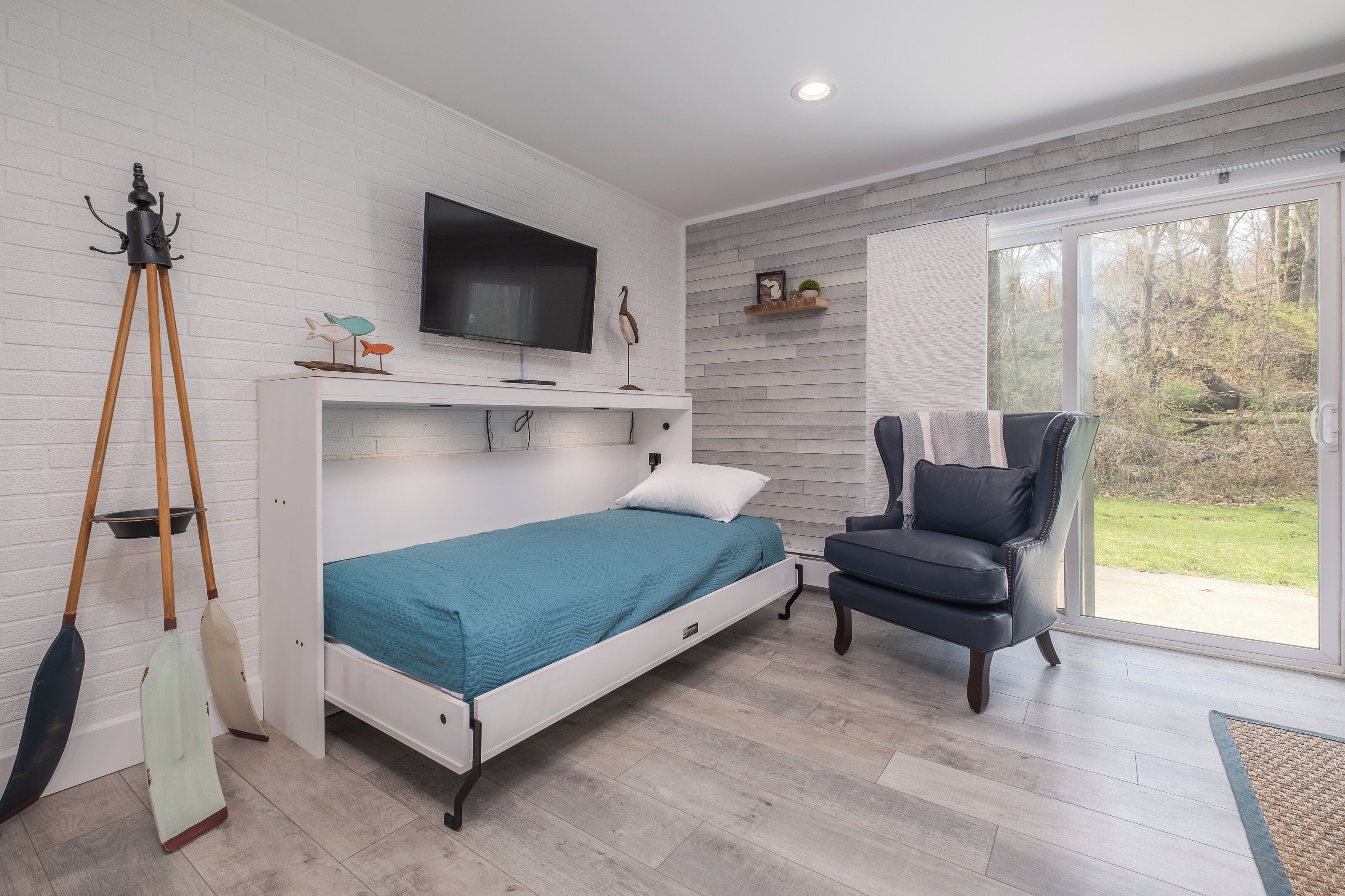 A modern bedroom with a bed, a television, a chair, and a view of the outdoors.