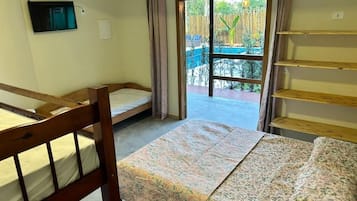A dormitory room with two bunk beds, a sliding door leading to a balcony, and a TV mounted on the wall.