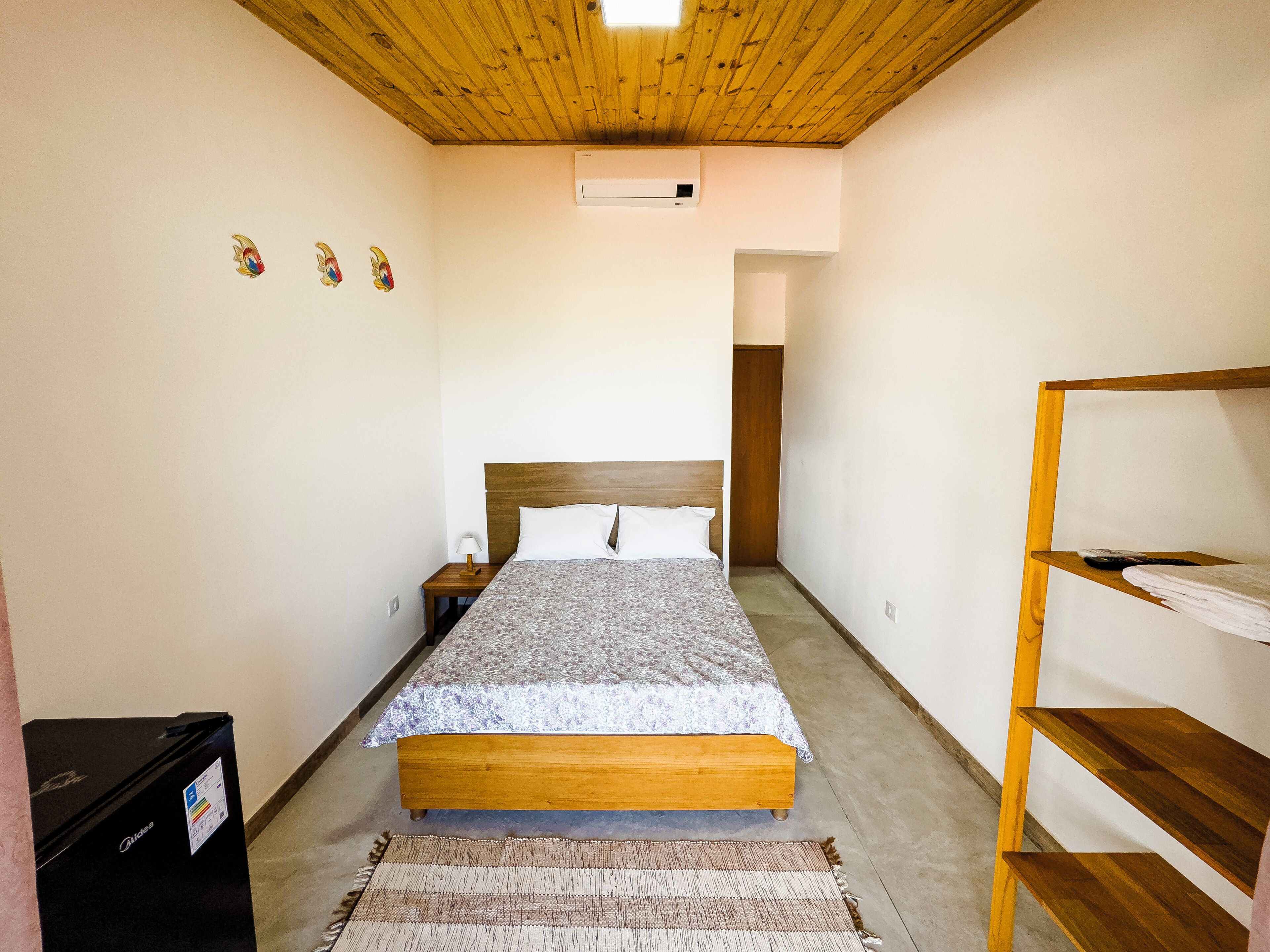 A bedroom with a wooden bed, a nightstand, a small heater, and a wooden shelf.