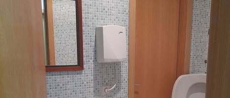 A bathroom with a tiled wall, a sink, a toilet, and a wooden door.