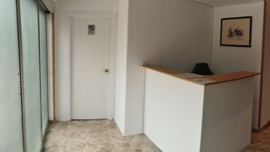 Een receptie met een balie, een deur met een ‘Niet roken’-bord, een ingelijst beeld aan de muur en een gang naar een andere kamer.