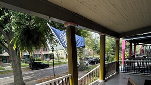 A covered outdoor seating area with a table and chairs, a view of the street, and a flag.