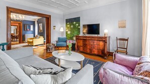 A spacious living room with a modern sofa, a blue armchair, a wooden cabinet, and a television.