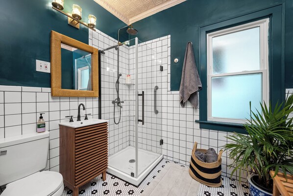 A bathroom with a shower, toilet, sink, and a mirror. - Spacious Historic 3-Bedroom Apt on Quiet Tree-Lined Street Near Peace Bridge (Buffalo)