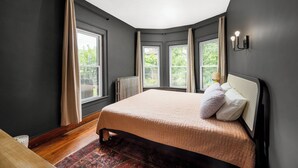 A bedroom with a large bed, a radiator, and three windows with curtains.