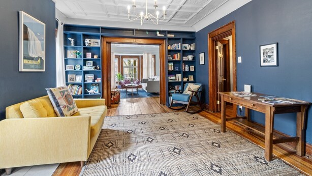 A room with a yellow sofa, a patterned rug, a wooden table, and a bookshelf filled with books and decorative items.