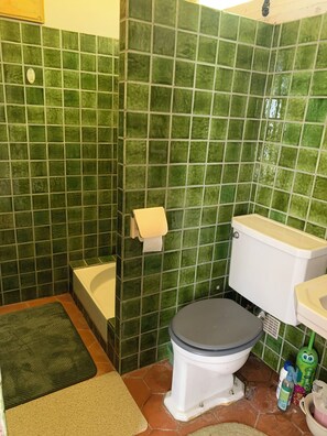 Casa de banho com paredes azulejadas verdes, sanita branca, banheira e lavatório.