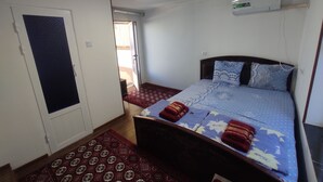 A bedroom with a bed, a door, a window, and an air conditioning unit. - Siyohkoron  (Bukhara)