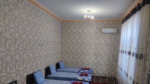 A room with four beds, each with blue bedding and decorative pillows. There is a red carpeted area and a white curtain on the right. - Siyohkoron  (Bukhara)