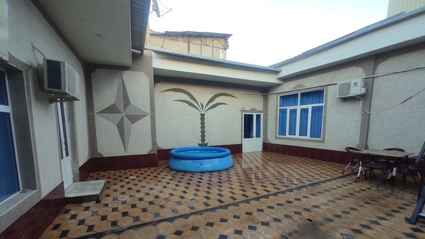 A courtyard with a patterned floor, a blue inflatable pool, and a dining area with a table and chairs. - Siyohkoron  (Bukhara)
