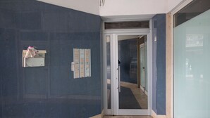 Een gang met een glazen deur naar een andere kamer, een klein schapje met spullen, en een prikbord met mededelingen.