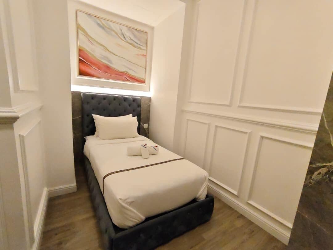A hotel room with a bed, a painting above it, and a marble wall.