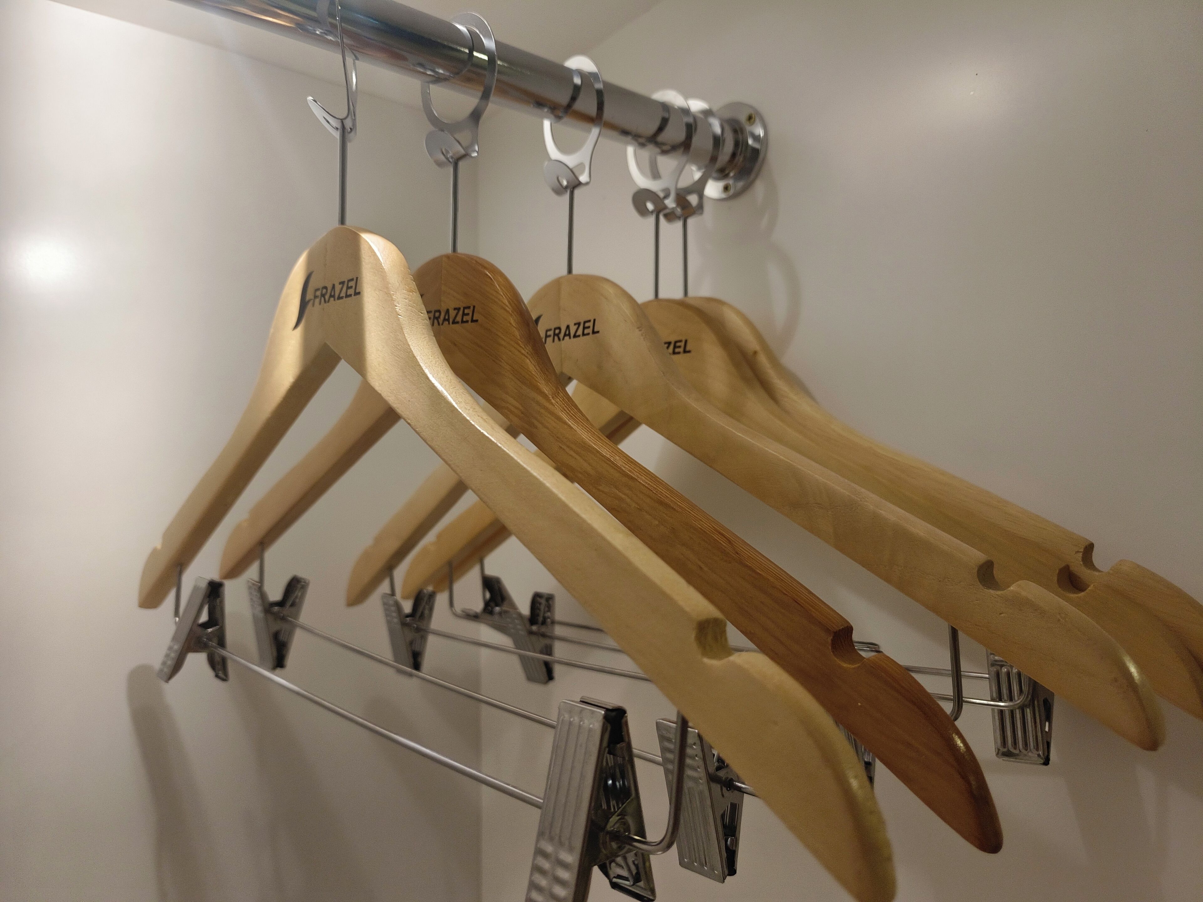 Perchas de madera con la etiqueta "FRAZEL" colgadas en un perchero de metal.