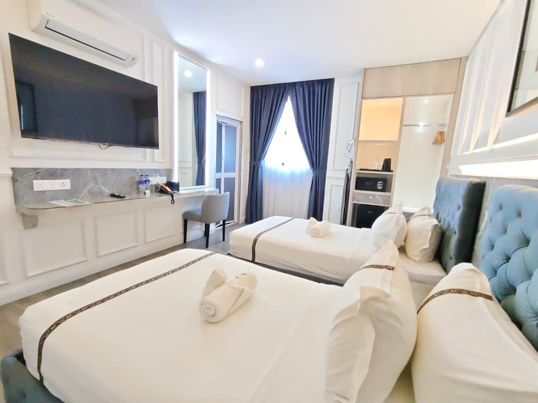 A hotel room with two beds, a flat-screen TV, a desk, and a blue upholstered headboard.