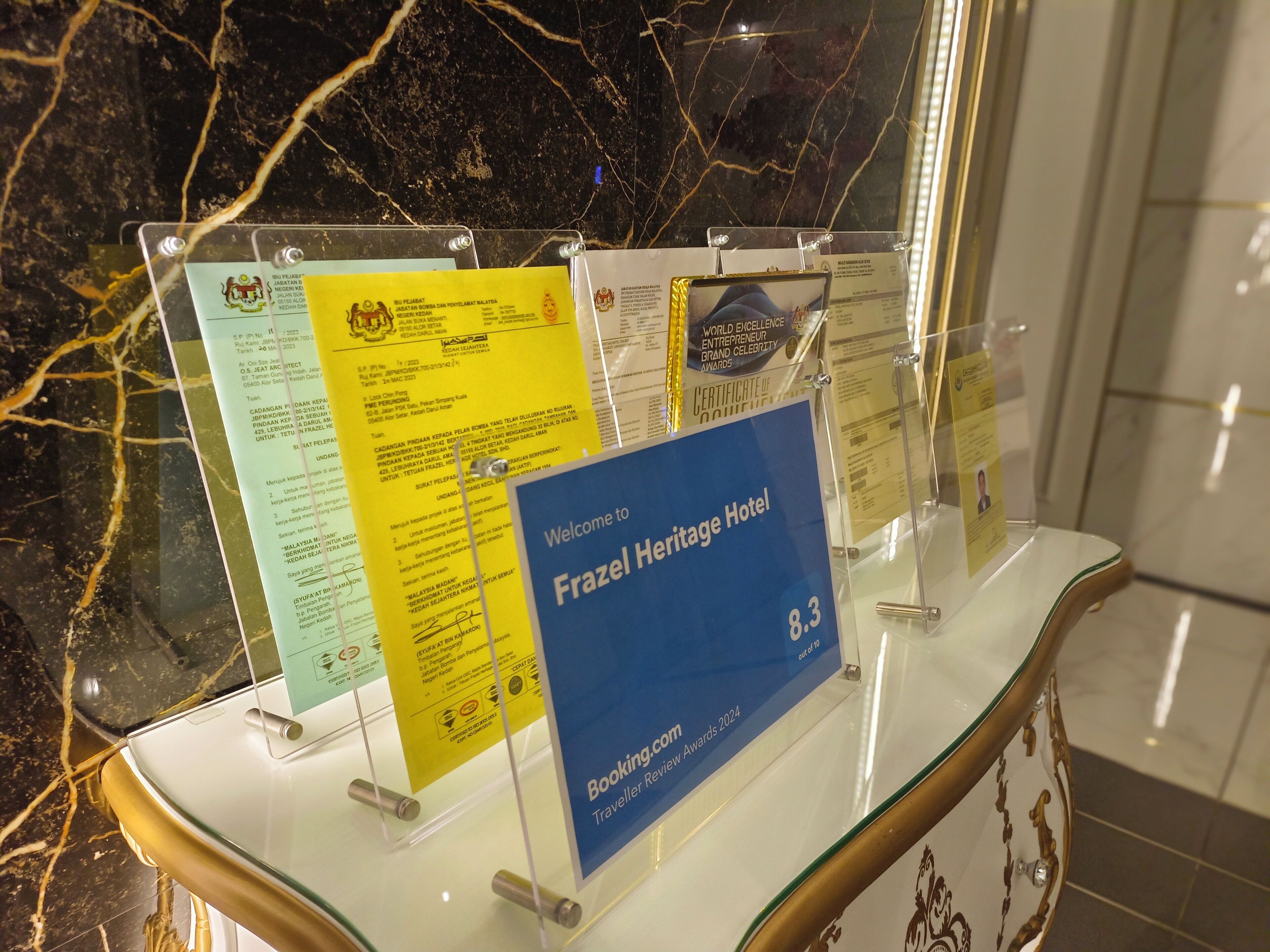 Une exposition de divers prix et certificats est présentée à l’hôtel Heritage, notamment un prix « Entrepreneur d’excellence mondiale » et une affiche annonçant les « Prix des avis des voyageurs 2024 ».
