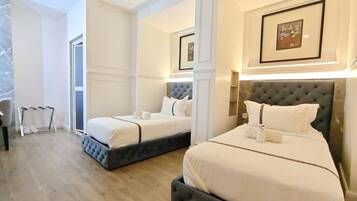 Quarto de hotel com duas camas, um espaço de estar e uma porta que dá para uma varanda.