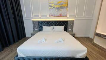 A hotel room with a large bed, a headboard with a tufted design, a painting above the bed, and a dark curtain on the left.