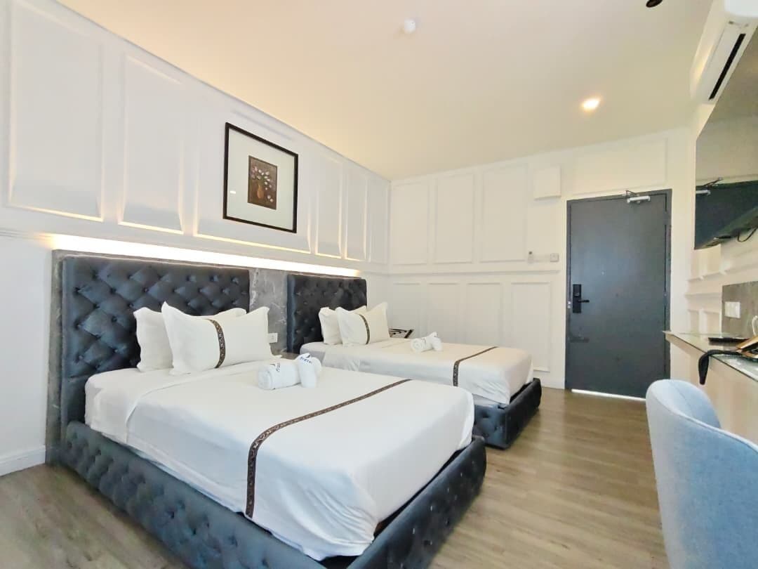Ein Hotelzimmer mit zwei Betten, einem dunklen Kopfteil, weißer Bettwäsche, einem gerahmten Bild an der Wand und einer Tür zum Badezimmer.