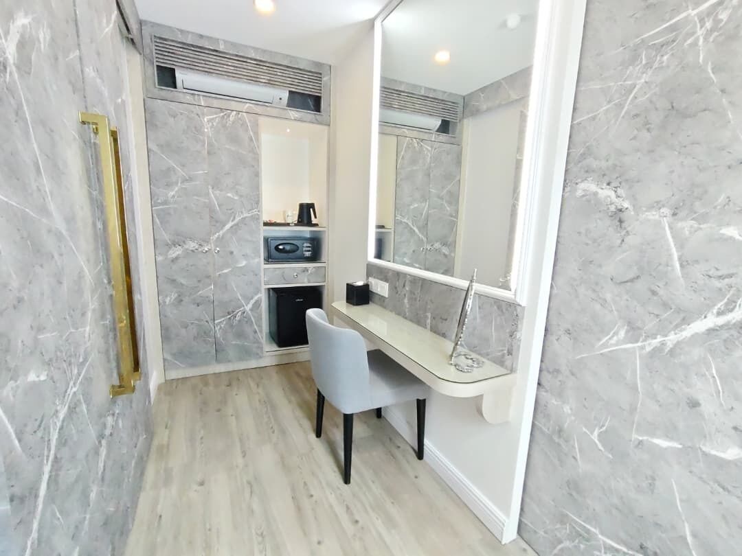 A bathroom with a marble wall, a shower area, a vanity with a mirror, and a chair.