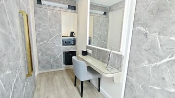 A bathroom with a marble wall, a shower area, a vanity with a mirror, and a chair.