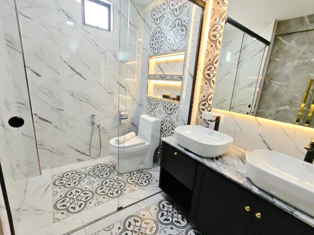 Un baño con piso de mármol, un lavamanos blanco, un espejo y un inodoro.