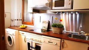 A compact kitchen with a washing machine, oven, microwave, and a sink with a stainless steel faucet. - Acogedor, Luminoso y Céntrico 2a (Madrid)
