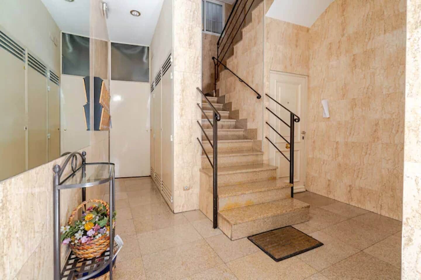 Una escalera con barandilla de metal, una puerta y suelo de baldosas.