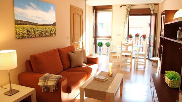 A living room with a sofa, a coffee table, a lamp, and a painting of a field. - Acogedor, Luminoso y Céntrico 2a (Madrid)
