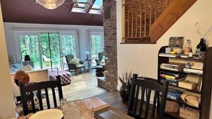 A dining area with a wooden table set for two, a bookshelf, and a staircase leading to an upper level.