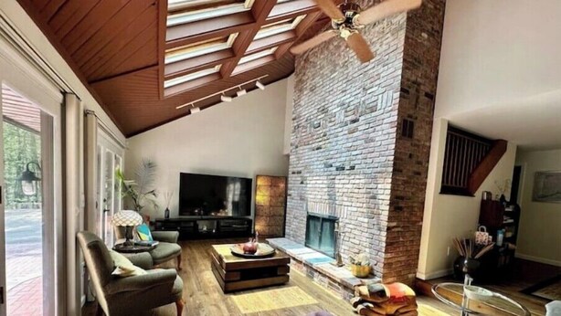 A spacious living room with a stone fireplace, wooden flooring, and a large TV.