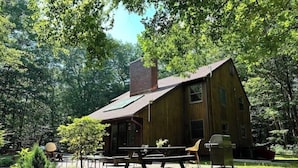 A rustic wooden cabin with a large deck, surrounded by dense forest.