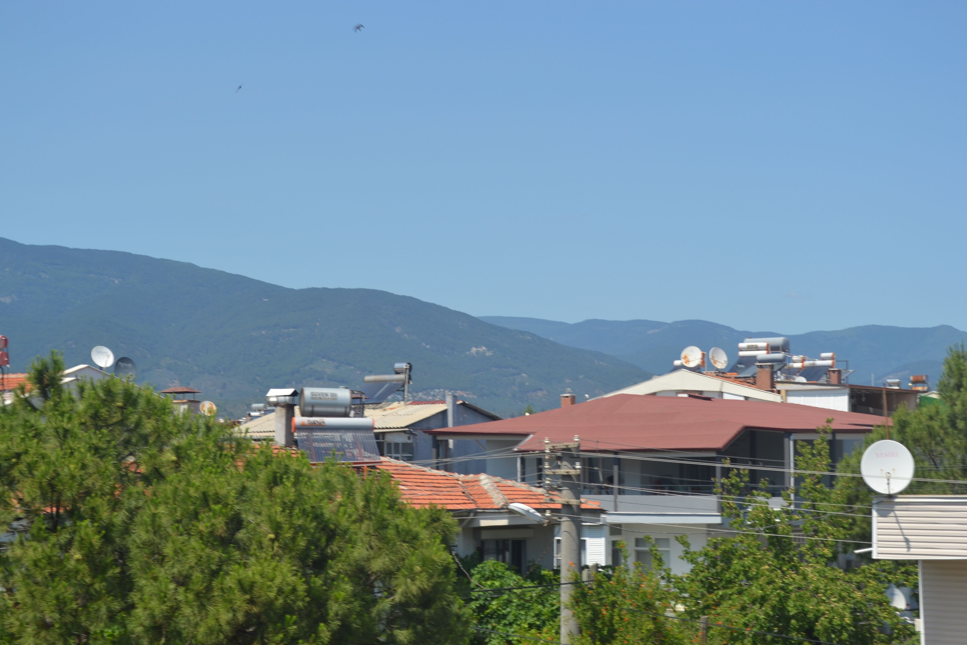 A residential area with houses, satellite dishes, and mountains in the background.