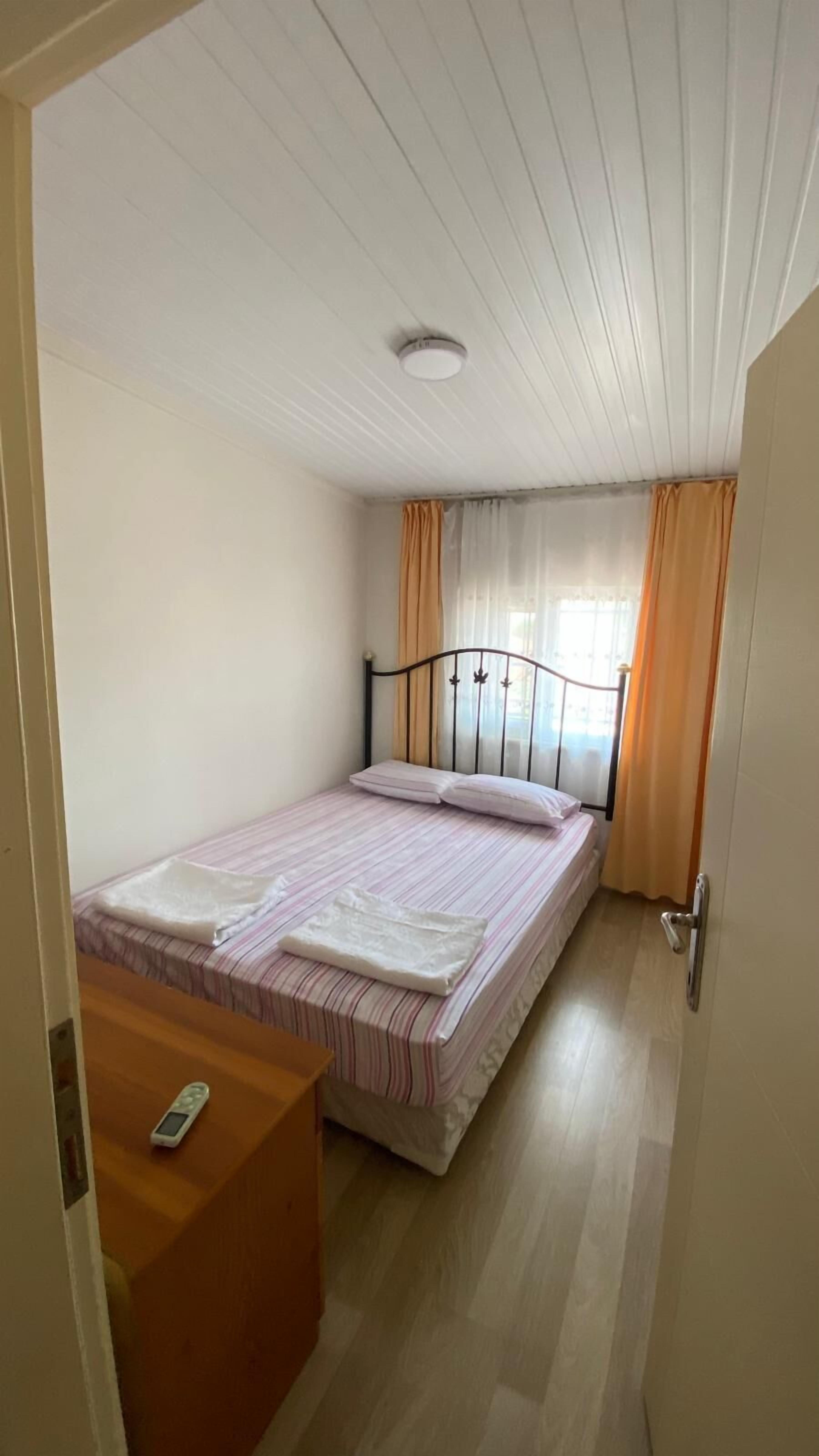Une petite chambre à coucher, bien rangée, avec un lit simple, une table de chevet et une fenêtre avec des rideaux.