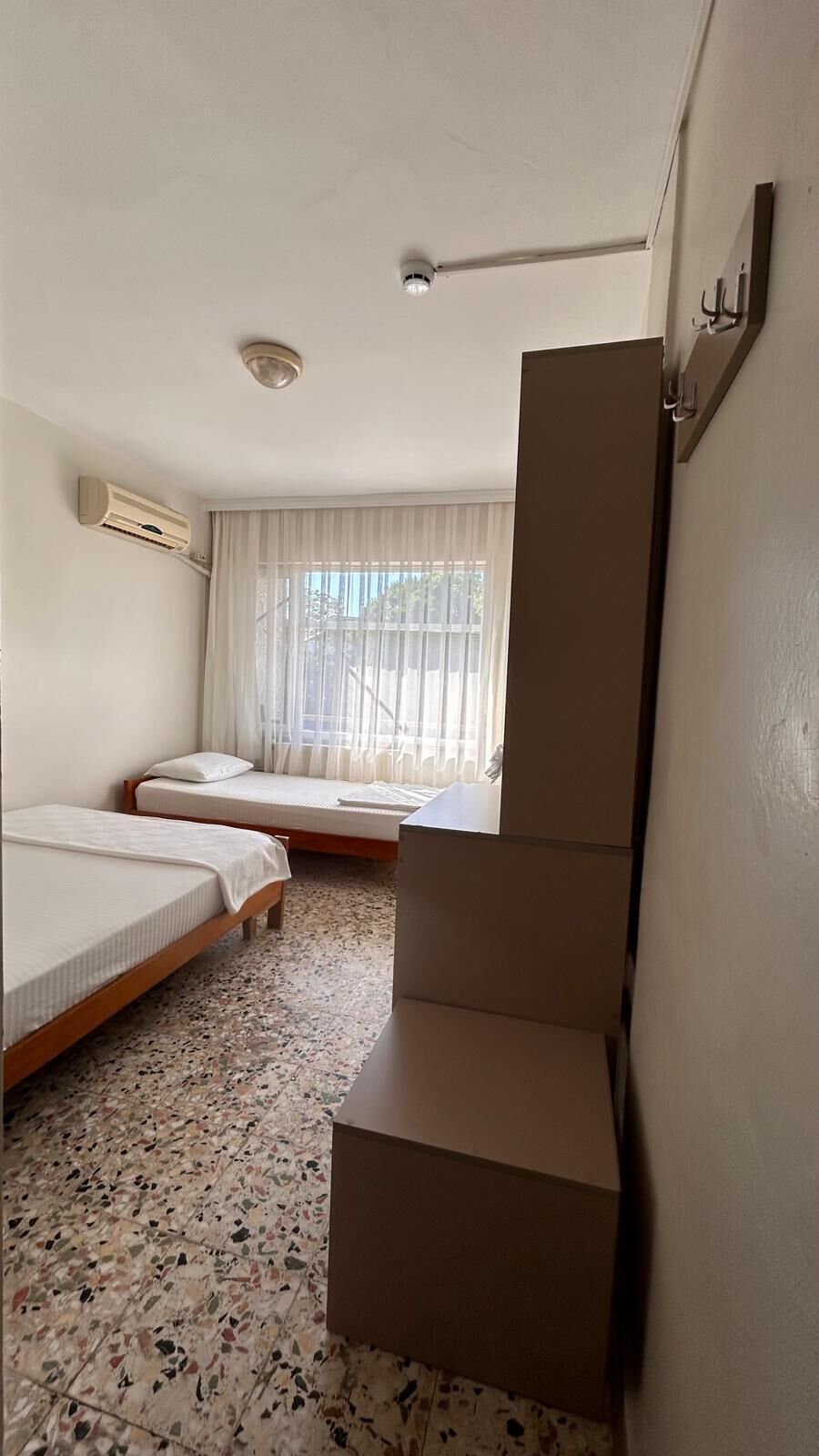 A room with two beds, a window with curtains, an air conditioning unit, and a staircase.