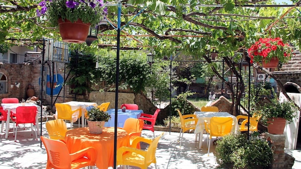 An outdoor patio with tables and chairs, surrounded by potted plants and a stone wall. - YAZICI (Edremit)