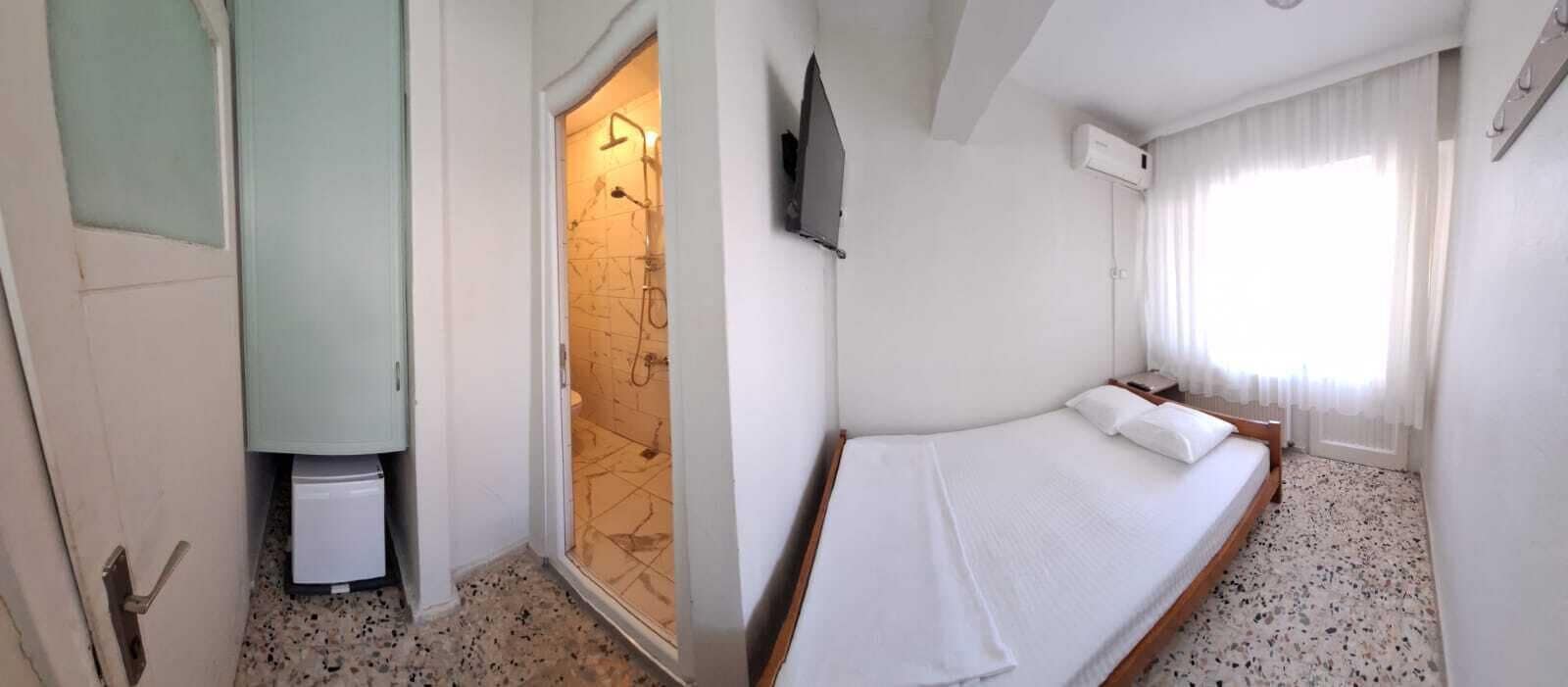 A hotel room with a bed, a shower area, a television, and a window with curtains.